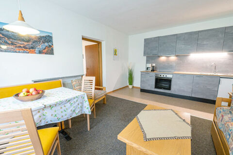 Modern kitchen and dining area with gray cabinets, wooden table, yellow chairs, and a fruit bowl at Residence Haus am Berg