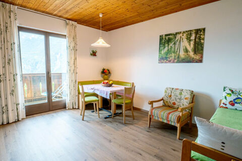 Dining area with green chairs, a table with a fruit bowl, floral armchair, and glass doors in Residence Haus am Berg