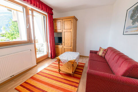 Living room in Residence Haus am Berg with red patterned sofa, wooden cabinet with TV, coffee table, and large window with balcony view