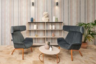 Two dark gray armchairs facing each other with orange legs, a round table with decor, and a shelf with vases at B&B Hotel Treviso Al Fogher