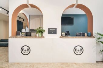 Reception desk with granite countertops and two arched openings, plants, computer monitors, and a TV screen at B&B Hotel Treviso Al Fogher