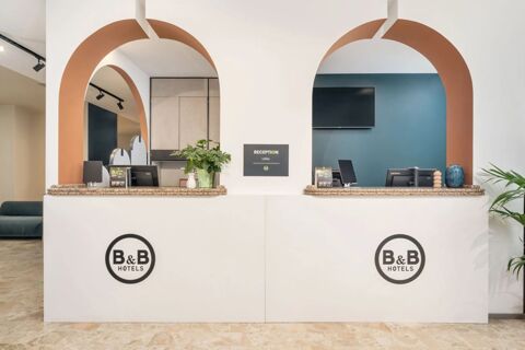 Reception desk with granite countertops and two arched openings, plants, computer monitors, and a TV screen at B&B Hotel Treviso Al Fogher