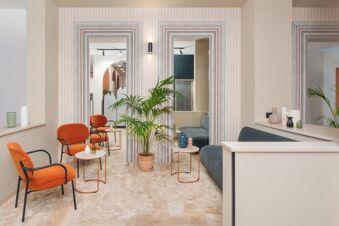 Seating area at B&B Hotel Treviso Al Fogher with orange chairs, small tables, a potted plant, mirrors, and blue sofas around the room