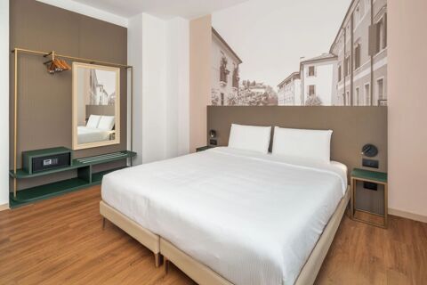 Minimalist hotel room at B&B Hotel Treviso Al Fogher with a double bed, white linens, wooden floor, and wall-mounted mirror with hangers