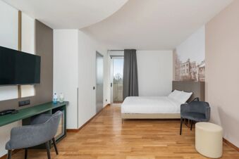 Hotel room at B&B Hotel Treviso Al Fogher with wooden flooring, a double bed, gray chair, green desk, and wall-mounted TV