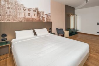 Modern hotel room at B&B Hotel Treviso Al Fogher with a double bed, nightstand, chair, ottoman, and wall mural above the headboard
