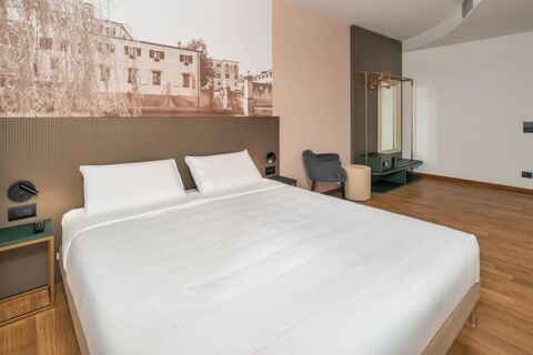 Modern hotel room at B&B Hotel Treviso Al Fogher with a double bed, nightstand, chair, ottoman, and wall mural above the headboard