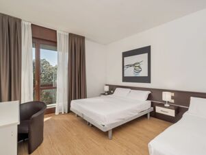 Guest room at B&B Hotel Eurorest Conegliano with two beds, wooden floor, nightstands, lamps, framed artwork, and a window with curtains