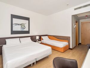 A hotel room at B&B Hotel Eurorest Conegliano with a double bed, a single orange bed, nightstand lamp, and wall art above the bed