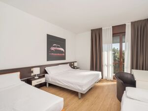 Room interior at B&B Hotel Eurorest Conegliano with two beds, a desk, a chair, a window, and a framed car picture on the wall
