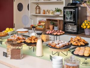 Breakfast buffet at B&B Hotel Eurorest Conegliano with croissants, doughnuts, cereals, milk, and a coffee machine on counter
