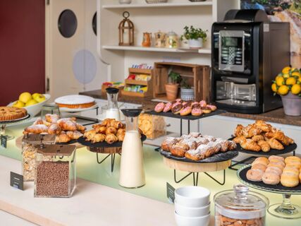 Breakfast buffet at B&B Hotel Eurorest Conegliano with croissants, doughnuts, cereals, milk, and a coffee machine on counter