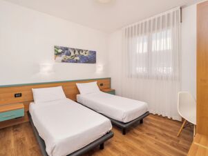 Two single beds with white linens, a wooden headboard, a wall painting, and sheer curtains at B&B Hotel Eurorest Conegliano