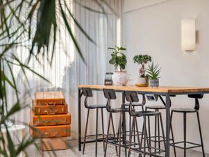 Stacked vintage brown suitcases next to a wooden table with black high chairs and potted plants in B&B Hotel Eurorest Conegliano