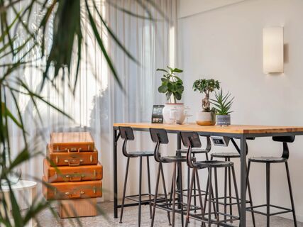 Stacked vintage brown suitcases next to a wooden table with black high chairs and potted plants in B&B Hotel Eurorest Conegliano
