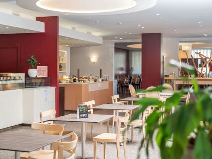 Dining area with wooden tables and chairs, a food counter, and red and white walls at B&B Hotel Eurorest Conegliano