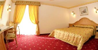 Przytulny pok&oacute;j w hotelu Torretta z podw&oacute;jnym ł&oacute;żkiem, ż&oacute;łtymi zasłonami i wykładziną w ciepłych kolorach.