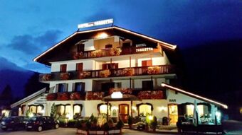 Oświetlony nocą hotel Torretta ma tradycyjną fasadę z balkonami i kwiatowymi dekoracjami w Alpach.