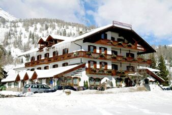Pokryta śniegiem fasada hotelu Torretta w g&oacute;rach z balkonami i widocznymi samochodami przed budynkiem.