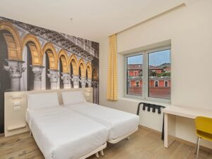 Two single beds with white bedding next to a wall with golden arches mural and window in B&B Hotel Milano Central Station