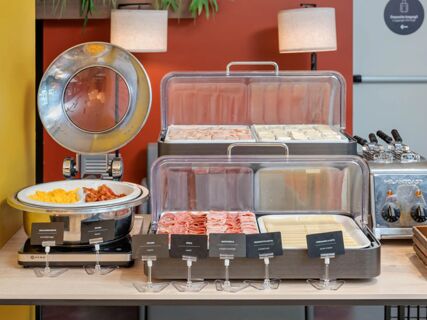 Buffet breakfast setup with scrambled eggs, bacon, cold cuts, sliced cheese, and sandwiches at B&B Hotel Milano Central Station