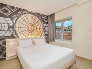 White bed with pillows against a wall featuring a large dome design next to a window with grey curtains at B&B Hotel Milano Central Station