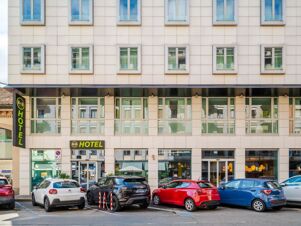 Facade of B&B Hotel Milano Central Station with large windows, hotel signage, and cars parked in front of the building