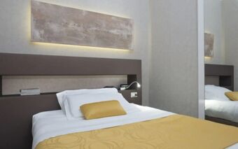A neatly made bed with white linens and a yellow pillow and blanket in a Hotel Atlantic room with abstract wall art