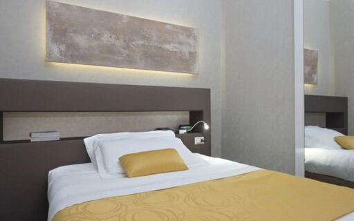 A neatly made bed with white linens and a yellow pillow and blanket in a Hotel Atlantic room with abstract wall art
