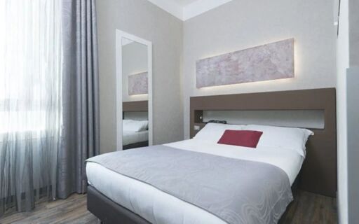 Minimalist hotel room at Hotel Atlantic with a double bed, gray curtains, a wall mirror, and abstract wall art above the headboard
