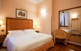 Hotel Berna room with a large double bed, padded headboard, bedside lamps, chair, full-length mirror, and hardwood floor