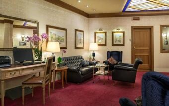 Hotel Berna lobby features leather seating, wooden desk with computer, decorative lamps, framed art, and floral arrangements