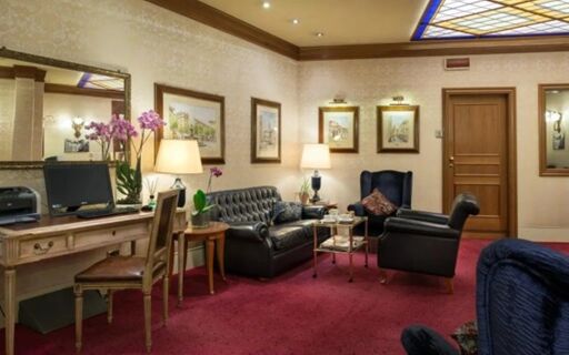 Hotel Berna lobby features leather seating, wooden desk with computer, decorative lamps, framed art, and floral arrangements