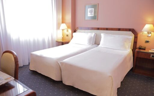 Hotel Bristol twin beds with white linens, wooden headboard, bedside tables, lamps, framed picture, and carpeted floor