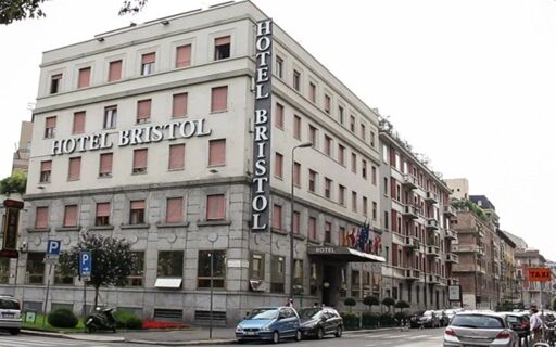Hotel Bristol is a multi-story building with a grey stone lower facade, pink window shutters, and a vertical hotel sign visible on a busy street in a city