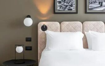 A neatly made bed with white pillows and quilted headboard in a room at Hotel Tocq featuring modern lighting fixtures