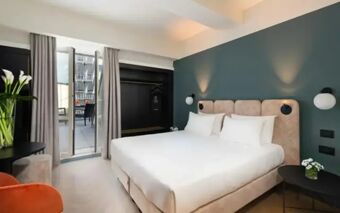 A modern Hotel Tocq room with a large bed, bedside tables, wall sconces, a closet, and a balcony with outdoor seating visible through glass doors