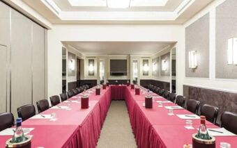 Meeting room at Doria Grand Hotel with tables covered in red cloth, black chairs, water bottles, and a TV screen on the wall