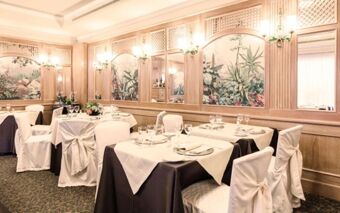 Dining area at Doria Grand Hotel with tables covered in white and black linens and wall murals reflecting nature scenes