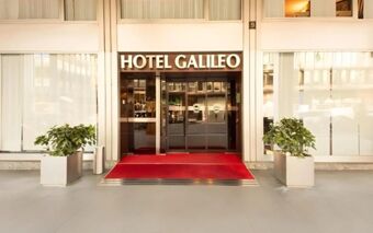 Entrance to Hotel Galileo with glass doors, a red carpet, and two large potted plants on each side