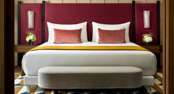 A neatly made bed with white linens, two pink velvet pillows, a mustard throw, and a burgundy headboard at Tivoli Tivoli President Milano Hotel