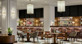 Seating area with tables, chairs, marble bar counters with brown stools, pendant lights, and shelves with bottles at Tivoli Tivoli President Milano Hotel