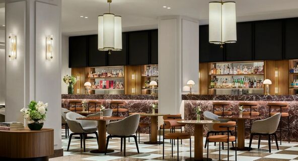 Seating area with tables, chairs, marble bar counters with brown stools, pendant lights, and shelves with bottles at Tivoli Tivoli President Milano Hotel