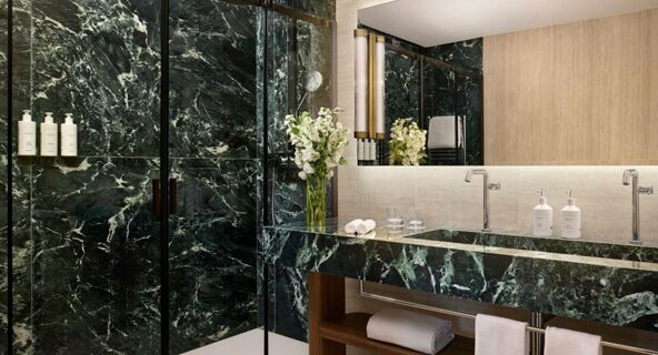 Modern bathroom with dark green marble walls, a glass shower, double sinks, white towels, and flowers at Tivoli Tivoli President Milano Hotel
