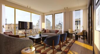 Living room with patterned rug, sofas, blue chairs, coffee tables, floor lamp, TV, and large windows with city view at Tivoli Tivoli President Milano Hotel