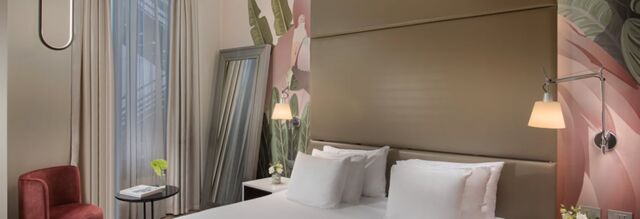 A modern hotel room at Hotel NH Collection Milano Touring with a large bed, white pillows, wall lamps, and a decorative mural wall