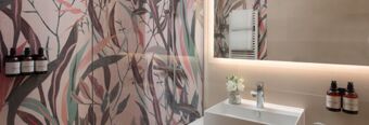 Shower area with colorful leaf-patterned glass panel, white sink with a flower vase, and toiletries at Hotel NH Collection Milano Touring