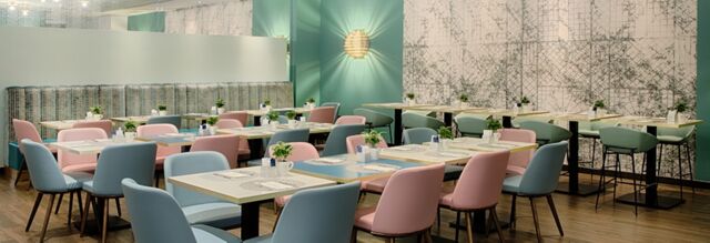 Dining area with pastel pink and blue chairs, patterned wallpaper, wooden floor, and small plants at Hotel NH Collection Milano Touring
