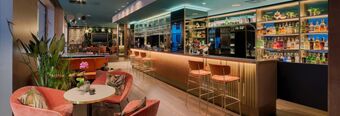 Interior view of the Hotel NH Collection Milano Touring bar with pink velvet chairs, round tables, plants, and bottles displayed on shelves behind the counter