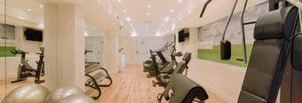 Fitness room with exercise bikes, weight bench, dumbbells, exercise balls, and wall mural at Hotel NH Collection Milano Touring